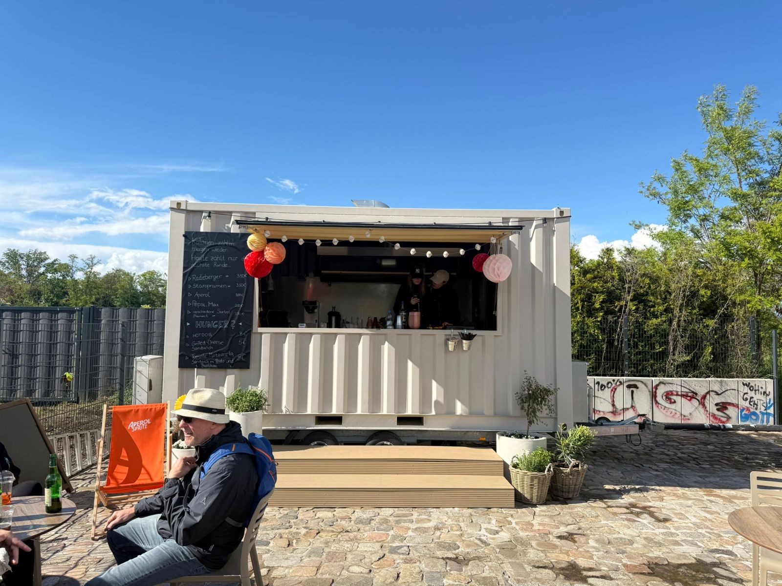 Container-Bar Bistro Brüggele an der Sternbrücke Magdeburg mit Gästen im Sonnenschein